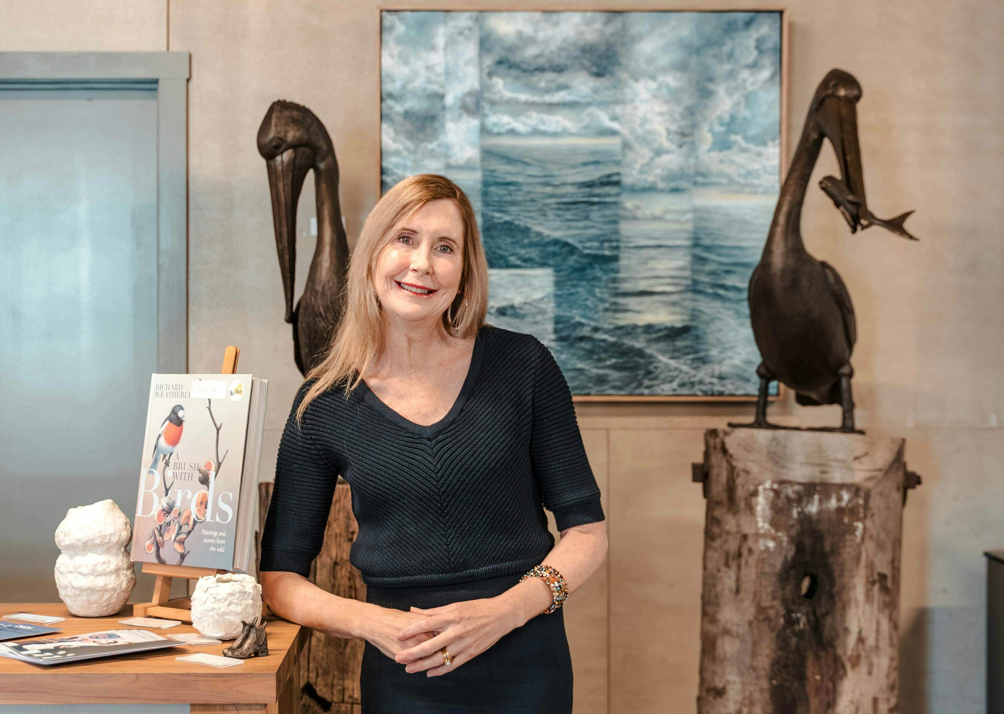 An artist beside paintings and bird sculptures featured in the Bellarine Arts Trail programme.