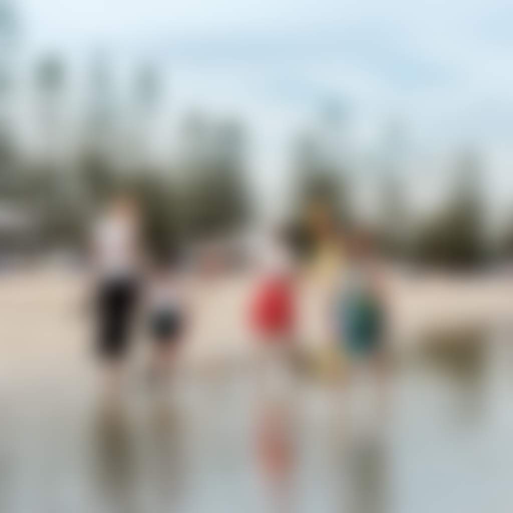 Family walking along Altona beach in water with pine trees in background